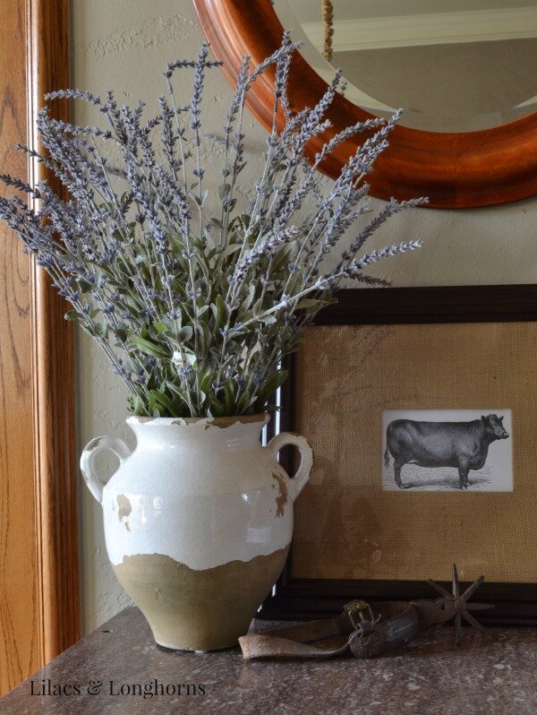 Faux lavender looks rustic and charming in this chippy urn nestled next to the cow print and cowboy spur.