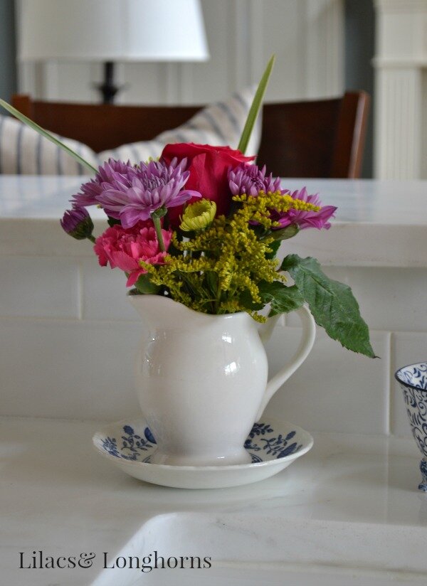 Brightly colored fresh flowers in a creamy white pitcher add a vibrant touch to the kitchen.